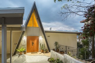 Set back on a quiet street, the orange double doors on the triangular facade echo the warm glow of light streaming through the window.