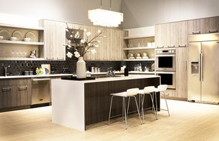 The Signature Kitchen Suite Cooking Demonstration Kitchen features maple wood cabinetry by Green Forest Cabinetry, Porcelain White countertops by LG Hausys, and a Virginia Tile backsplash by Lunada Bay. A West Elm chandelier hangs over the island, adding a touch of drama.