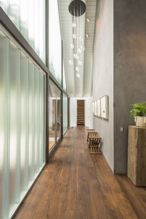 The glass facade of the residence invites light into the living room while a fireplace doubles as a privacy screen. Wide plank, hand-distressed walnut flooring runs throughout the home, which is comprised of two main wings flanking an open, communal space. From this view, you can see steps leading above the garage into an attic space that is currently set up as a home theater.