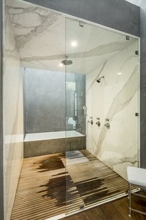 A deep soaking tub complements a shower lined with marble and wooden slats. A double vanity sits opposite.