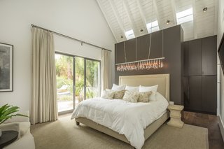 Like all the bedrooms and bathrooms, the master bedroom has electric venting skylights, as well as a sliding door that leads to the back patio. "Sleeping at night, you can throw the doors and the skylights open, and you get beautiful, natural circulation into the house," says Van Scoter. Behind the bed is a dark wood wardrobe that feeds into the en suite bathroom.