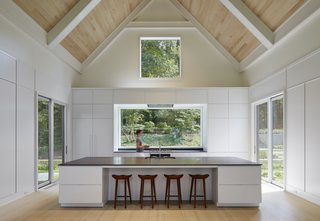 Cabins and Connectors Form a Family’s Lake Michigan Retreat - Photo 4 of 6 - Two smaller sliding doors lead outward from the kitchen, which continues the home's minimalist aesthetic. Booth Hansen chose to paint the window interiors white to match the neutral color palette. "When you're looking out the windows, the house takes a backseat to the environment," says Sandschafer.