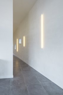 From a constricted entryway without a lot of natural light, the passageway fans upwards towards the landscape. Throughout the home, simple neon lights on unpainted plaster walls produce a warm glow. Explains Alireza Razavi, director of Studio Razavi Architecture, "The Dan Flavin-ist quality of the neon bulbs perfectly lit the space without focusing your attention on the fixture."