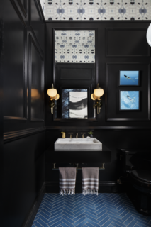 Designed by Benni Amadi Interiors and Courtney Springer Interiors, the "Moody Blues" powder room and vestibule pairs a marble sink with dramatic black walls that make the room seem more spacious, while blue tiles laid in a herringbone pattern reference the traditional architecture of the home.