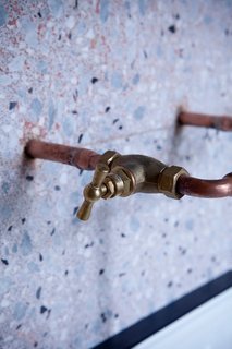 Copper piping for faucets extends out from a terrazzo-covered bathroom.
