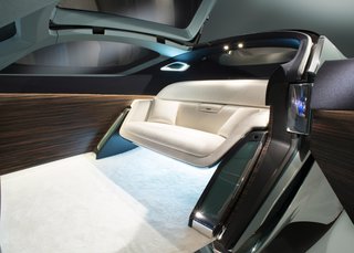 Interior details include an expansive OLED touch-screen, Macassar wood paneling, deep-pile ivory wool carpet, and a silky wool sofa. A luggage compartment is hidden near the front wheels.
