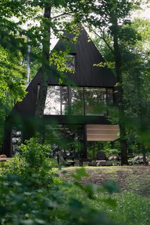 15 Modern Homes with Black Exteriors - Photo 9 of 15 - Jean Verville architecte designed FAHOUSE, a residence burrowed in the middle of a hemlock forest in Eastern Townships, Canada. The design takes inspiration from the archetypal figure of a house and doubles it with two triangular prism forms that are connected – almost like two trees growing towards the sky.