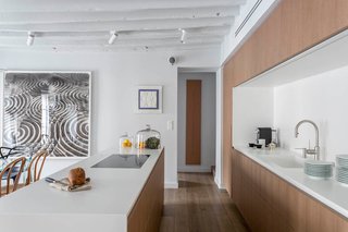 The subtle palette of white and wood is broken up by pops of color and pattern provided by the collection of the homeowner's artwork, which is strategically placed throughout the space for maximum impact.