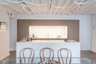 A blend of old and new marks the renovation of this apartment in Paris, where historic wood beams were painted white to emphasize their texture, and wood veneered cabinets were selected for the kitchen. Even the vintage Thonet dining chairs are paired with a more contemporary glass dining table.