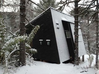 This winter retreat located in a forest in the Araucanía Region of Chile was designed by MC2 Arquitectos to face a small waterfall. One side features a large window, while the other walls has smaller windows that focus on specific views and provide ventilation for the house. Its painted brown exterior helps it blend into the surrounding landscape.