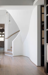 9 Unique Stair Railings - Photo 4 of 9 - An undulating spiral stair with a white railing on one side and a slim wooden handrail on the other connects the upper and lower floors of a renovated home in Australia. The bends of the railing mimic the curves of the building's exterior, and the wood handrail is recessed into the wall, tracing a path upwards.