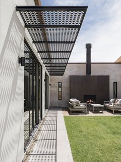 A custom-cut steel awning with a perforated pattern casts shade on a glazed wall.