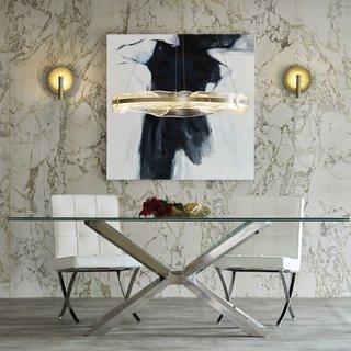 Glass-covered wall sconces illuminate either side of an art piece and act as a visual connector to the glass dining table and textured glass pendant over the table.
