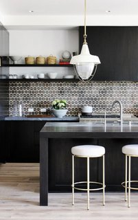 In this kitchen by DISC Interiors, the stark black cabinets and kitchen island are offset by light whitewashed floors and white-and-brass accents. To finish off the look, a patterned ceramic tile backsplash packs a punch. 