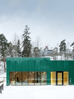 The bold, emerald hue complements the cemetery's lush surrounding gardens. The green glass reflects the surrounding vegetation, integrating the building into the garden spaces framed by the cemetery’s hedges.