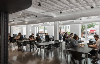Employees eat at tables in a large entry space with plenty of windows and natural light.