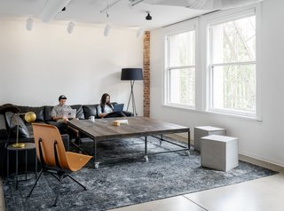 Large tables, modern plywood chairs, and neutral tones offset the white and brick to make a comfortable, open space to work in.
