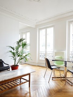 In the 11th arrondissement, the elegance of wood chevron floors, delicate crown molding, and ceiling medallions is balanced by stark white walls and ceilings and a select few pieces of furniture, allowing the white French doors and views to the outside to take priority.