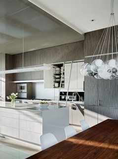 The backsplash consists of two anodized aluminum door panels that lift up via specialized hardware. It also contains a built-in spice cabinet and recessed steam oven, and provides access to an array of cooking utensils, cookware, and oils. A custom anodized aluminum ladder rail also offers access to the upper storage. 