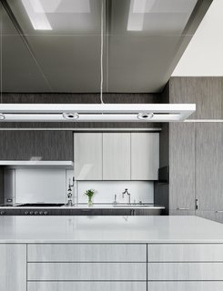An overhead lighting fixture by ALW hangs above the island's gray/white stained engineered oak, which contrasts with the cabinet's darker gray engineered oak.