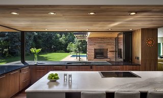 The Kemps wanted to emulate a European-style kitchen that would be minimal in appearance, but highly functional. Their induction cooktop is centered in an island of white Calcutta marble. Custom base cabinets at the island have a cool gray automobile paint finish. The perimeter countertops are fabricated from absolute black granite while the walnut base cabinets continue the classic mid-century vibe. A sleek folding panel window system allows the kitchen to have full exposure to the exterior. 