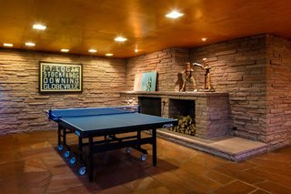 The rumpus room delighted the Kohn<br>family, with its sprawling fireplace,<br>television seating, and honed-flagstone<br>arena for ping pong—a sport the<br>current owners of One Eudora also<br>enjoy. The articulated wood figures<br>on the mantel, made for a gym in the<br>early 20th century, were used to teach<br>children how to box. The framed vellum<br>is a historic Denver-area trolley sign.
