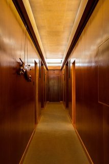 A long clerestory illuminates the hallway dividing the bedroom<br>wing of the house. The door at the end originally opened to racquet storage and<br>pathway access to a subterranean tennis court. The carved greyhound dates to<br>the 1920s.