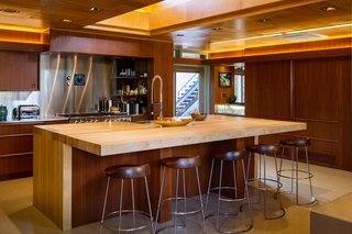 The renovated kitchen honors architectural precedents<br>in the house, including lighting coves, crescent<br>drawer pulls, and match-grained cabinetry doors<br>that roll along the same hardware used in 1947. The<br>clerestory directs light onto the maple island, whose<br>proportions and structure pay homage to the dining<br>room’s original table. Even the terrazzo recalls the<br>feeling of the first flooring material—asbestos tile—<br>which was abated for safety. 