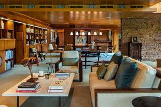 Warmth permeates the living room,<br>where Honduran mahogany paneling,<br>bookshelves and built-ins stand<br>sumptuously in concert with birch<br>ceiling tiles, all caramelized with age.<br>Jeffrey P. Elliott executed the interior<br>design, weaving in the homeowners’<br>quirky collection of art, objects and<br>furnishings—no easy task considering<br>the Marianna von Allesch glass mural<br>juxtaposed with a toy monkey shaking<br>a martini. The striped chair in the<br>background is a rare Victor Hornbein<br>commission, one of a pair. The sculptural<br>staircase seems to float in place, belying<br>its satisfying weightiness underfoot.<br>A thin metal edge inserted into the<br>hardwood tread prevents slipping<br>and beautifully punctuates the Lou<br>and Romy Bieker design.