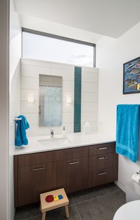 Inside Out - Photo 7 of 7 - A light-enhancing transom window in the kids’ bathroom mimics the high-floating windows in the adjacent bedroom. Large-scale gray floor tiles and sleek cabinetry contrast with the playful vertical stripe in the tile ("the owners wanted a little bit of color and pop," says Goff); the hue mimics a teal blue seen throughout the home. Remove the children’s stool, and the bath will become sophisticated enough for a teen—or beyond. 