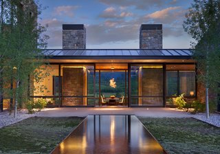 CRESCENT H – Situated on top of a sloping knoll and an aspen grove, this home was sited to capture panoramic mountain views and create a dramatic arrival sequence. The program is arranged in separate building forms to cultivate intimacy while maximizing exposure. Movement is choreographed to contrast solid characteristics with void, creating pockets of shelter and outdoor connections. The roof protecting the kitchen pavilion, along with the kitchen and dining rooms, lays across an east-west axis to take full advantage of the scenery. Sedimentary stone from a nearby quarry mimics the natural landscape, with clear vertical grain cedar siding to break up the pattern and add warmth. Photo by Gibeon Photography.