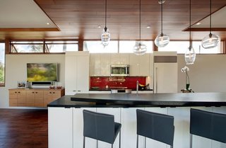 The floorplan of the home strategically places the primary living spaces including the kitchen, living room, and master bedroom on the second floor, maximizing the user's exposure to views as well as the surrounding tree canopy. Wood ceilings, floors, and window frames are paired with stark white walls and bold accent colors to juxtapose modern architectural detailing with a sense of warmth and intimacy. 