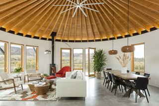 The largest of the three yurt structures houses the living and dining rooms and provides panoramic views. A geometric hide rug by Dedalo Rugs ties in pops of red from Eero Saarinen's Womb Chair, and pale blue from the Room and Board cushions on the sofa. The homeowners sourced the Oggetti Showtime coffee table from Wayfair. A pair of Kichler pendants define the dining area.