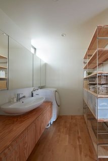 In a Japanese home designed by Koizumisekkei, mirrors and a slim shelf made of raw wood and metal line one side of the wall, creating the illusion of expansiveness in the laundry room.