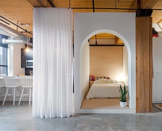 This small L-shaped apartment has a bed box with an arched doorway, white walls, and plywood finishings.