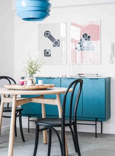 Tiles with colored grouting and a metallic blue cabinet with geometric graphics are some of the unique features of this home. A bedroom is hidden behind a television cabinet that merges with the open kitchen.