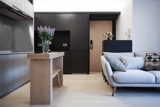 A fuss-free monochromatic color palette works beautifully with unvarnished wooden floors, blown-glass pendants, and sleek stainless-steel kitchen counters. A slim wooden island counter with just enough space for an elongated bench serves as a food preparation area and doubles up as a tiny dining table. 