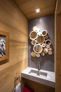 Nature is present throughout the interiors of this French Alpine home, including in the bathroom, where the cross section of tree trunks serve as frames in a cluster of small mirrors. 