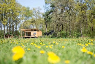 Overlooking a peaceful meadow in the province of Overijssel in the Netherlands is a snug, 452-square-foot prefabricated wooden hut with large windows that blur the boundaries between indoor and outdoor spaces. Build in two modules that were transported and assembled on site, the house, which was constructed mainly with Oregon pine, arrived complete with bathroom, kitchen, couches, table, inner walls, cabinets, beds, and floors. Custom-designed furniture, such as a sofa integrated into a sunken living area, and a U-shaped corner bench, imbues this little hut with plenty of quirky charm.
