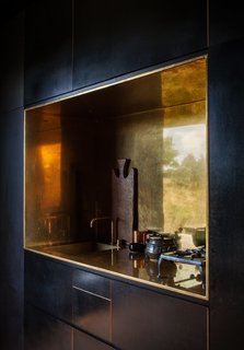 This off-the-grid cabin in New Zealand features a kitchen niche that's lined with polished brass. It works seamlessly with a tap by Arne Jacobsen for Vola that perfectly contrasts the otherwise spare, black, and minimalist interiors.