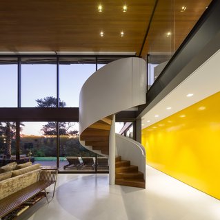 Calling to mind the iconic Barcelona Pavilion, this glass-encased home demonstrates the power of simple geometric forms. A sculptural, white spiral staircase ascends to a mezzanine where a media room, fitness room, and balcony are located. 