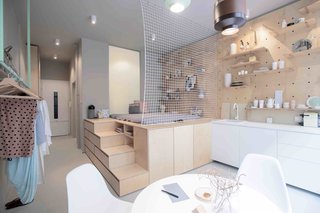 To maximize space in this tiny 323-square-foot studio Budapest apartment, local design studio POSITION Collective used an elevated, plywood sleeping unit inspired by Japanese "tansu" mobile cabinetry, with secrete storage modules on the side of the steps leading up to the futon bed.