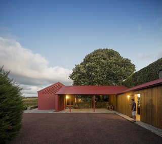A Bright Red Island Residence Embraces a Linden Tree - Photo 1 of 13 - A wide, open-air, stone-paved corridor connects two volumes.