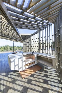 The latticework of the screens allows light to enter the porches, casting ever-shifting shadows as the sun moves across the house through the day. On the side porch is an outdoor grilling area that's perfect for entertaining. There are also multi-level benches arranged around the fire pit where friends family can gather. 