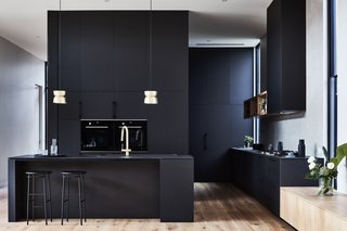 The sleek black kitchen is fitted with oak timber floors and brass accents to infuse additional sophistication into the space.