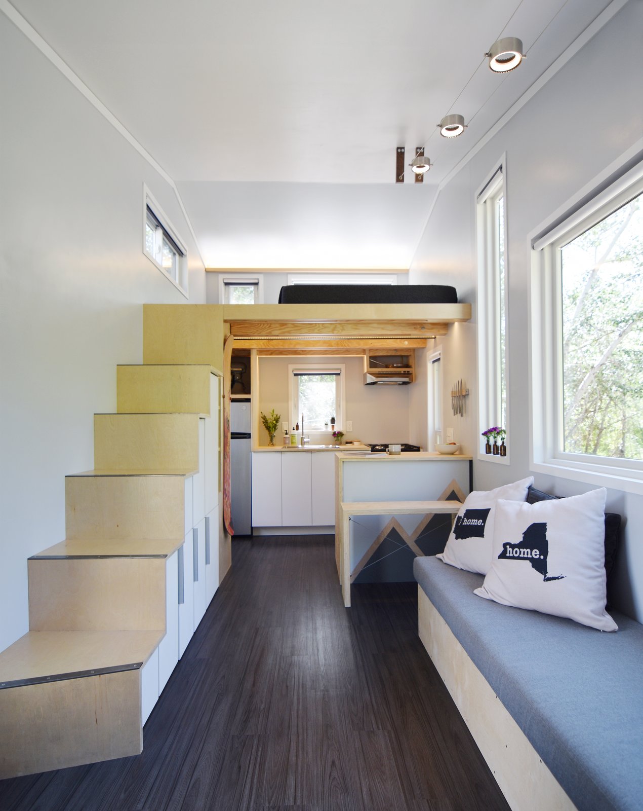 The kitchen is fitted with a compact propane stove cook top and oven, refrigerator, a sink, and a pantry behind the stairs.