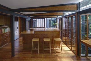 At the center of the house, on the upper level, is a kitchen and dining area fitted with glazed walls that can be opened to connect with the outdoor decks and green landscape.