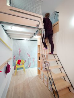 On the main level, the designers created an alcove playroom for the children. This area doubles as storage space for the kid's toys, so the main living area can remain clutter-free. From the alcove playroom, a ladder leads up to a mezzanine loft with a double-bed and two single beds.