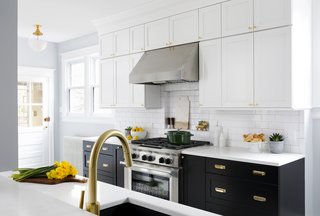 A classic subway tile backsplash with contrasting grey grout and stacked cabinets with matte brass hardware and fixtures emphasize the classic feel of the home. The new cabinets include pull-out pot and pan drawers, a waste and recycling compartment, pantry roll-outs, a spice pull-out, and base tray storage. 