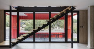 The interior staircase cuts diagonally across the floor-to-ceiling windows.